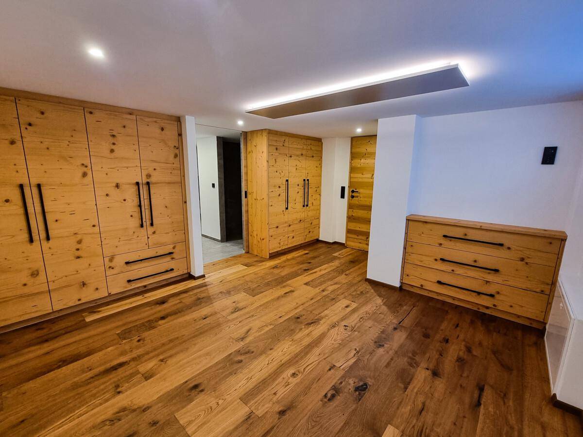 Geräumiges Schlafzimmer mit maßgefertigten Holzschränken, Holzboden und indirekter Beleuchtung.