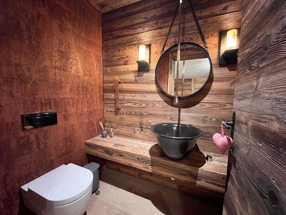 Elegantes Gäste-WC mit Holzwänden, modernem Waschbecken und rundem Spiegel.