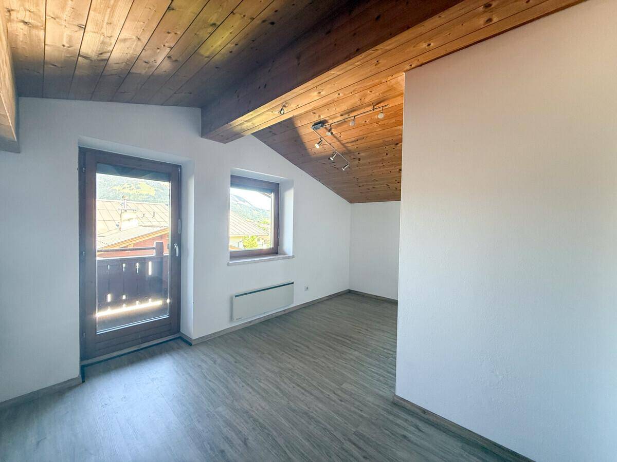 Gemütliches Dachzimmer mit Holzbalkendecke, Laminatboden und Zugang zu einem kleinen Balkon.