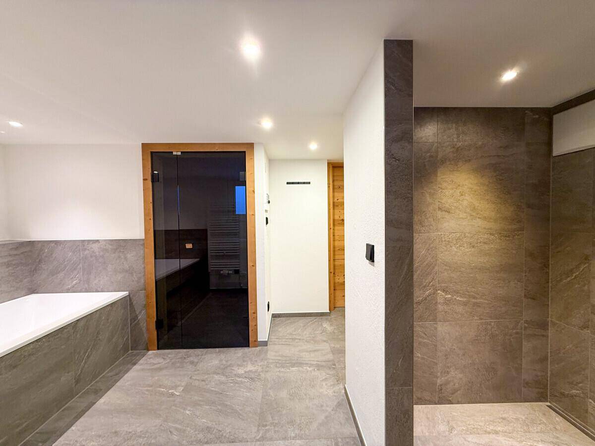 Modernes Badezimmer mit Fliesenboden, begehbarer Dusche und direktem Zugang zur Sauna.