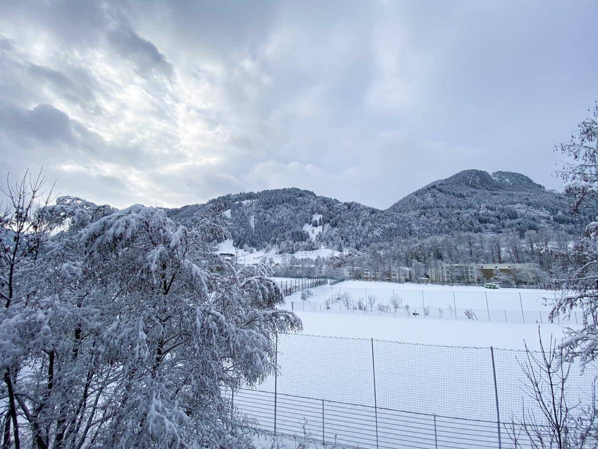 Winterliche Landschaft mit schneebedeckten Bergen und Bäumen unter bewölktem Himmel.