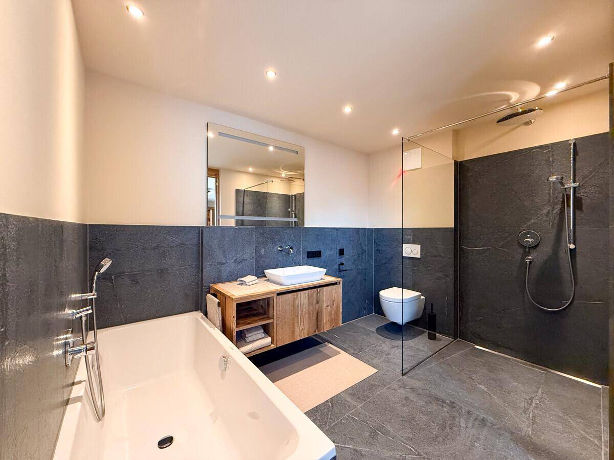 Geräumiges Badezimmer mit Badewanne, begehbarer Dusche, Waschtisch und großem Spiegel.