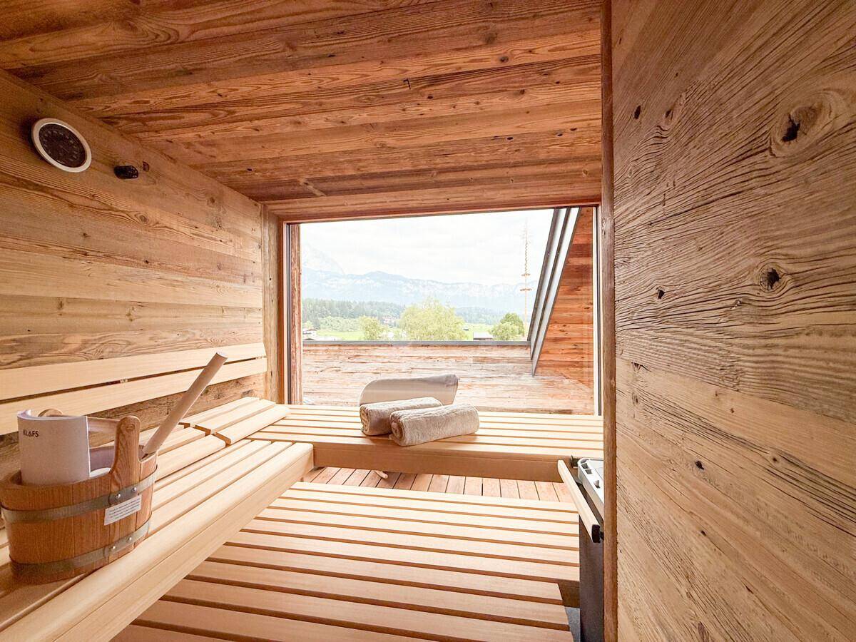 Geräumige Holzsauna mit Sitzbänken und großem Fenster mit Bergblick.
