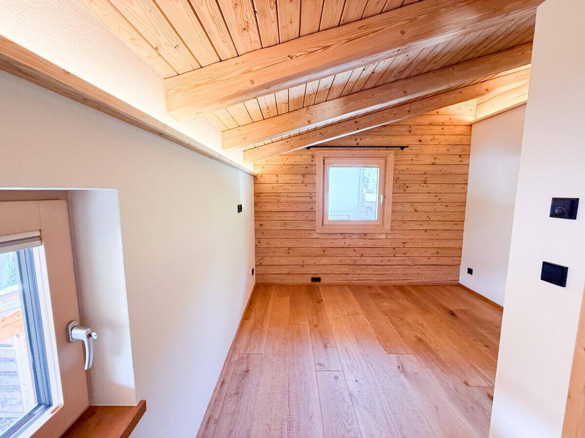 Helles Zimmer mit Holzwänden, Holzboden und schräger Decke, ideal als Schlaf- oder Arbeitszimmer.