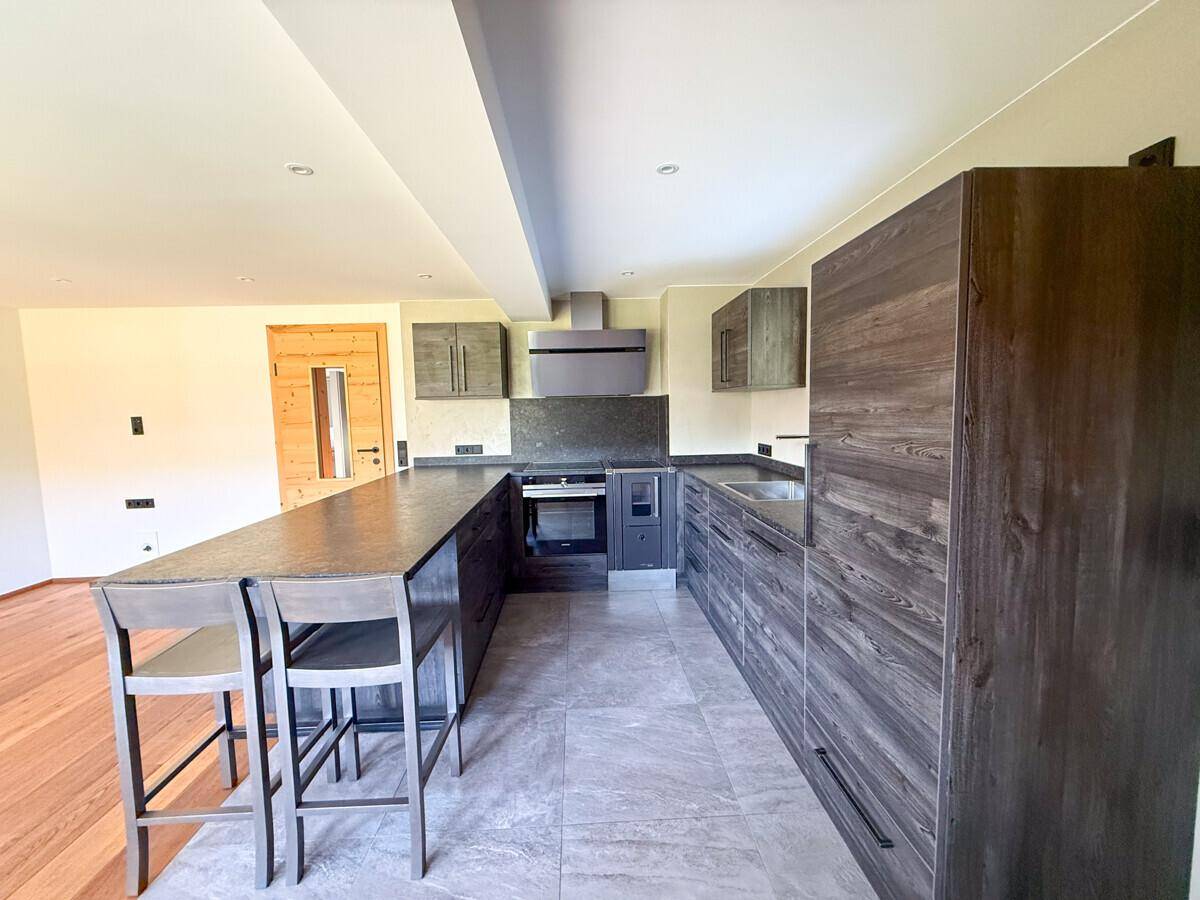Moderne Einbauküche mit dunklen Holzfronten, Kücheninsel und hochwertigen Geräten in offenem Design.