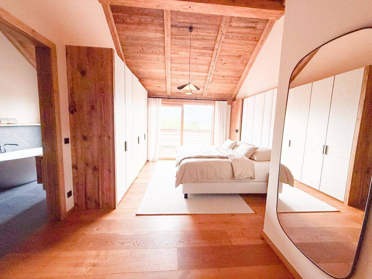 Helles Schlafzimmer mit Holzbalkendecke, Einbauschränken und Zugang zu einem Balkon.