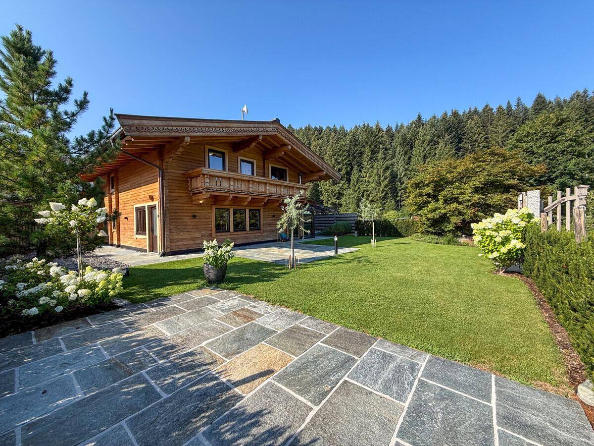 Charmantes Holzchalet mit gepflegtem Vorgarten, Rasenfläche und traditionellem Balkon.