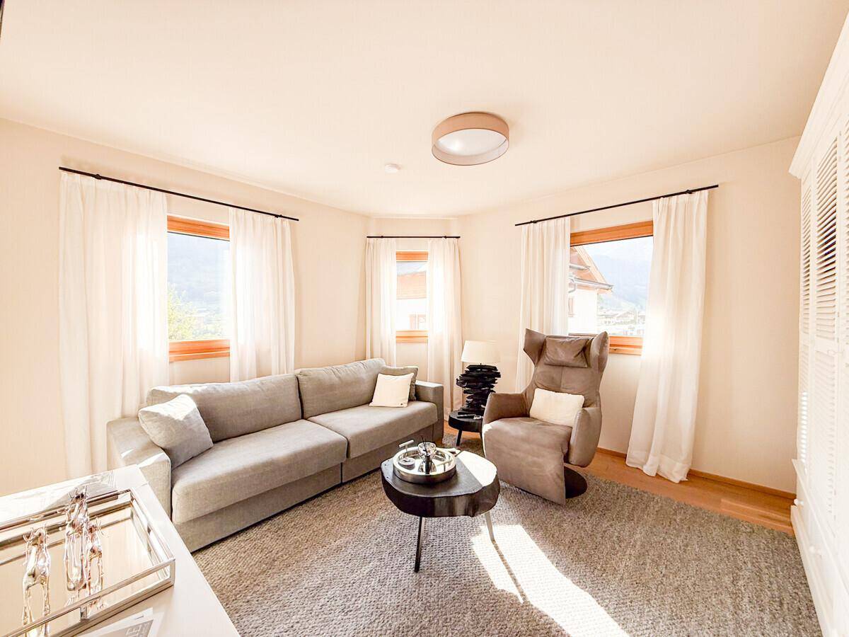 Gemütliches Wohnzimmer mit bequemer Couch, Sessel und großen Fenstern für viel Tageslicht.