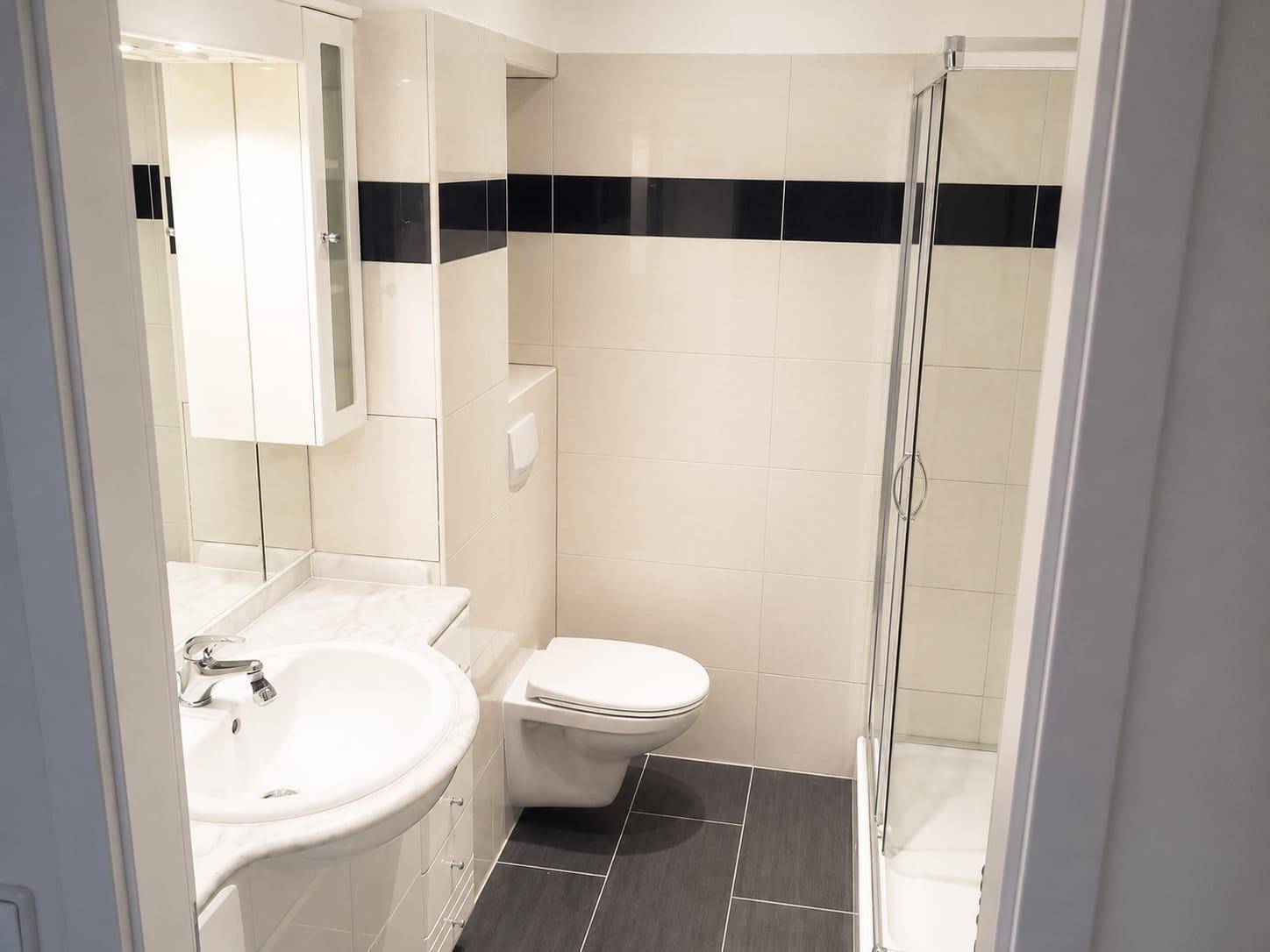 Modernes Badezimmer mit Dusche, WC, Waschbecken und weißen Fliesen mit dunklem Akzentstreifen.