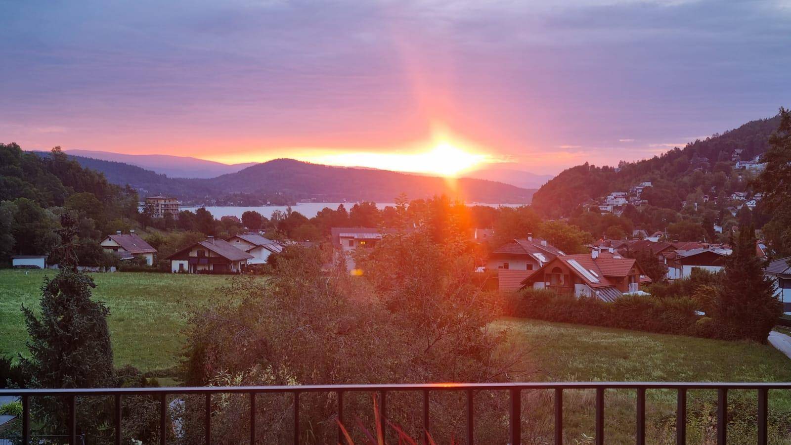 Atemberaubender Sonnenuntergang über einem See mit Bergpanorama und Blick auf die umliegende Wohngegend.