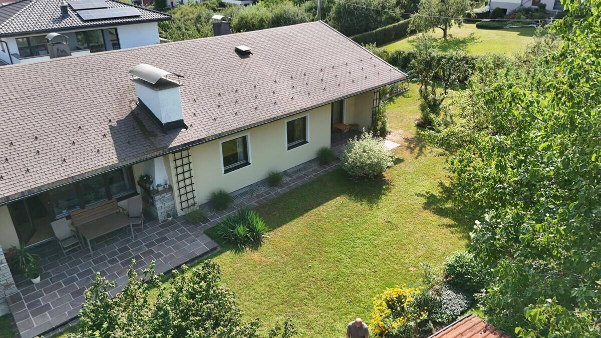 Rückansicht des Hauses mit großer Rasenfläche und gepflasterter Terrasse.