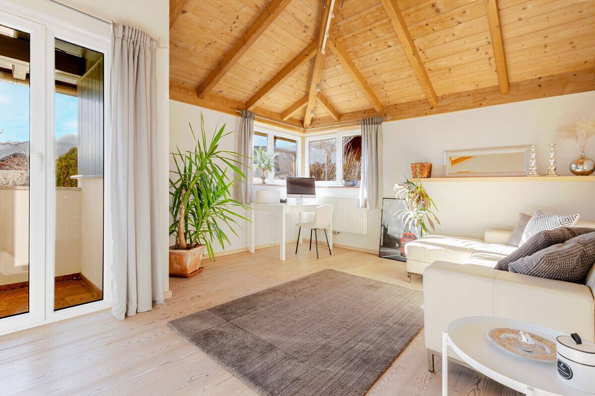 Lichtdurchfluteter Raum mit Holzdachschräge, Arbeitsbereich und Zugang zu einem kleinen Balkon.