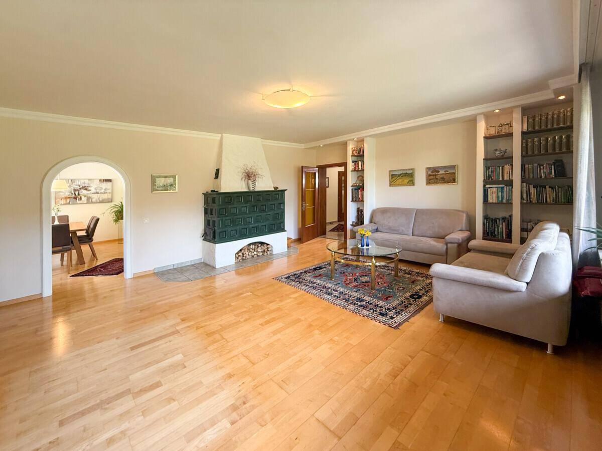 Geräumiges Wohnzimmer mit Kachelofen, Parkettboden und integrierten Bücherregalen.