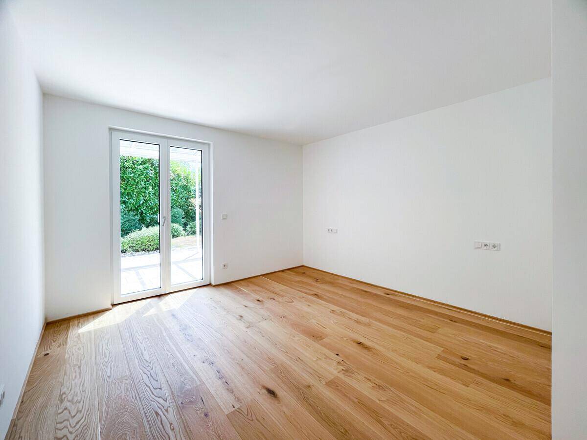 Lichtdurchfluteter Raum mit Holzboden und direktem Zugang zum grünen Außenbereich.