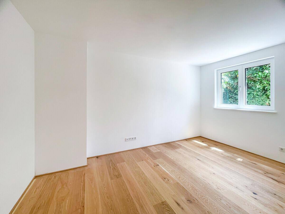 Ruhiges Zimmer mit Holzboden und einem Fenster mit Blick ins Grüne.