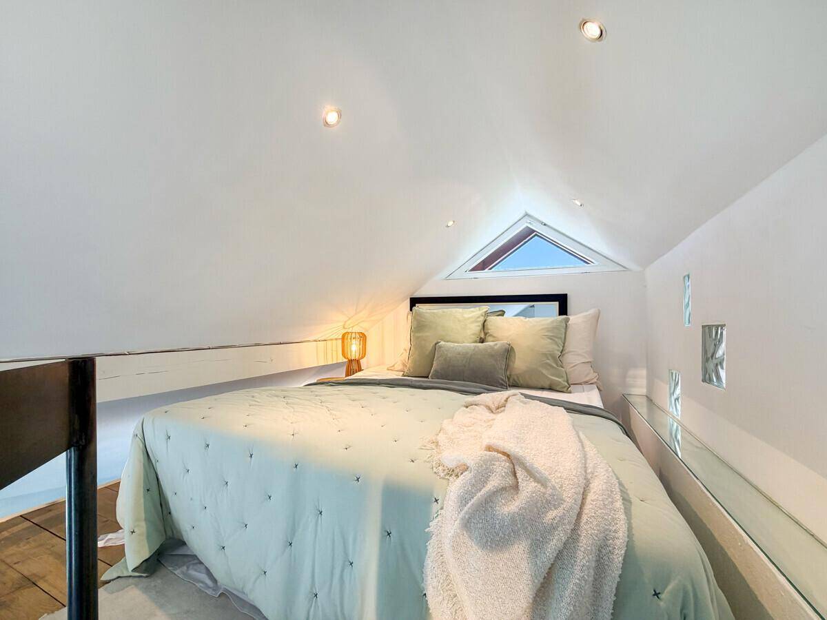 Gemütliche Schlafgalerie mit Bett, schräger Decke und kleinem dreieckigen Fenster.