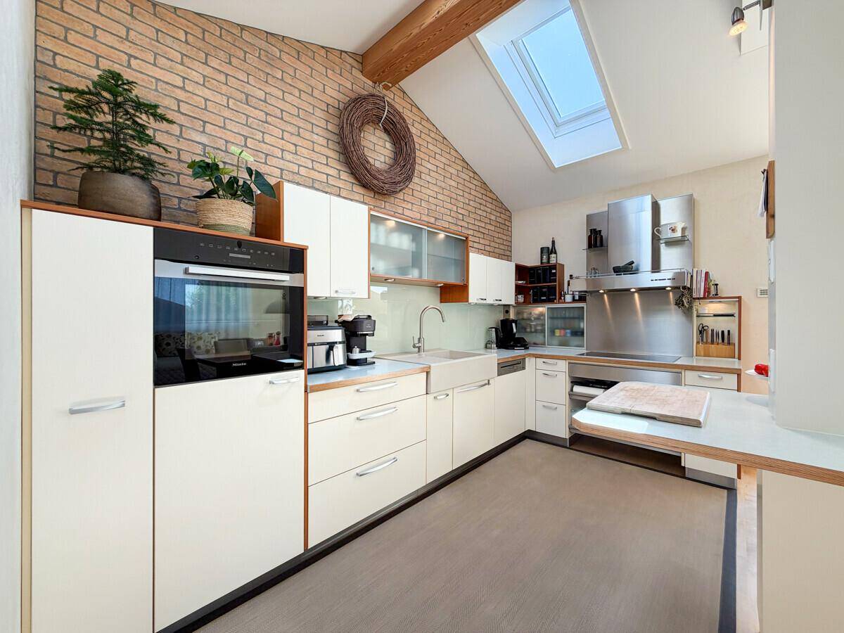Helle Einbauküche mit Backsteinwand, modernen Geräten und Dachfenster für viel Tageslicht.