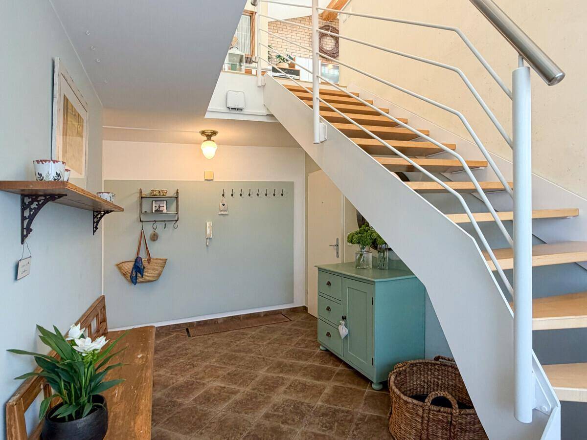 Heller Eingangsbereich mit Treppe, Fliesenboden und einer Garderobe.