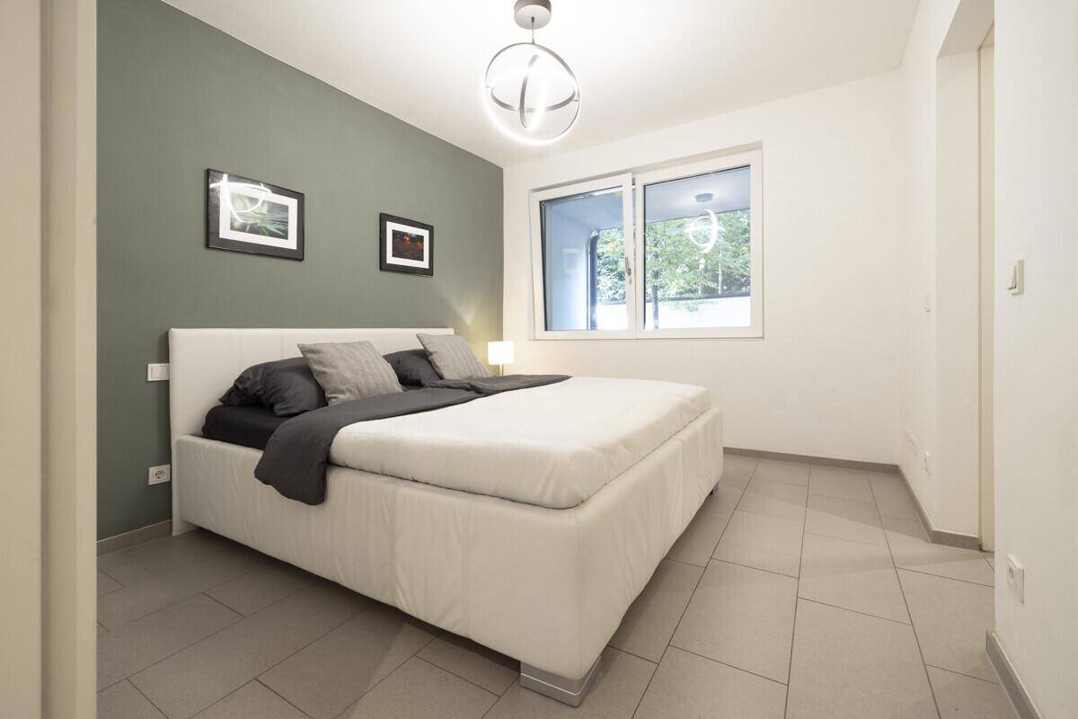 Schlafzimmer mit modernem Bett, grauer Akzentwand und Fliesenboden.