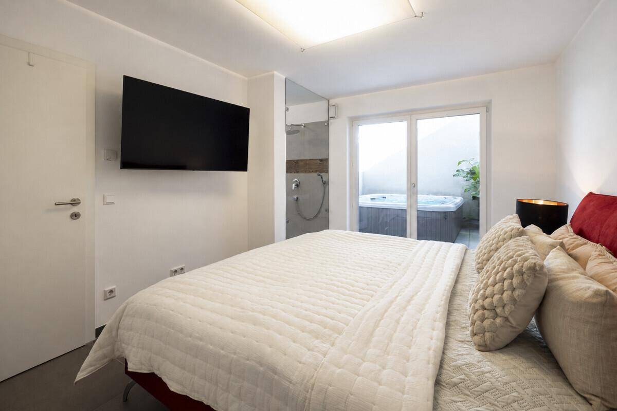 Gemütliches Schlafzimmer mit großem Bett, Wandfernseher und Blick auf den Whirlpool im Freien.