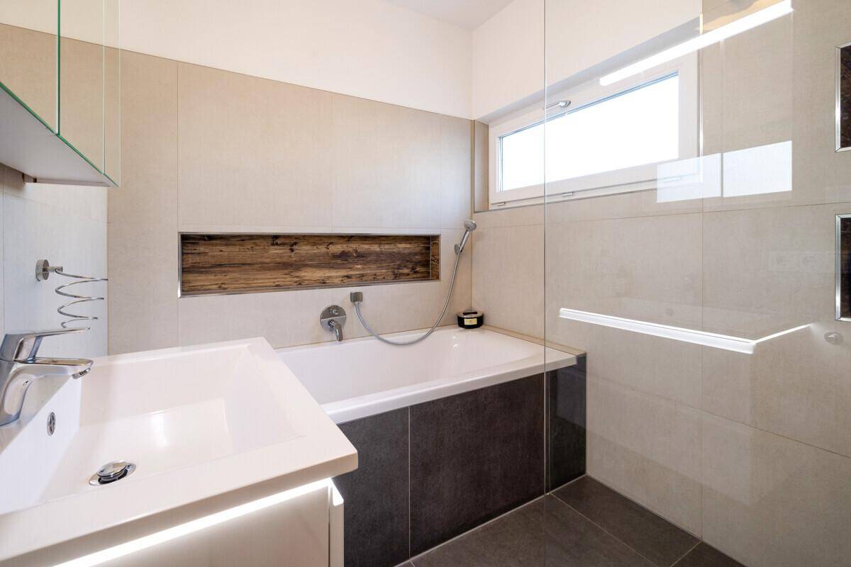 Modernes Badezimmer mit Badewanne, Waschtisch und Fenster für natürliche Belüftung und Tageslicht.