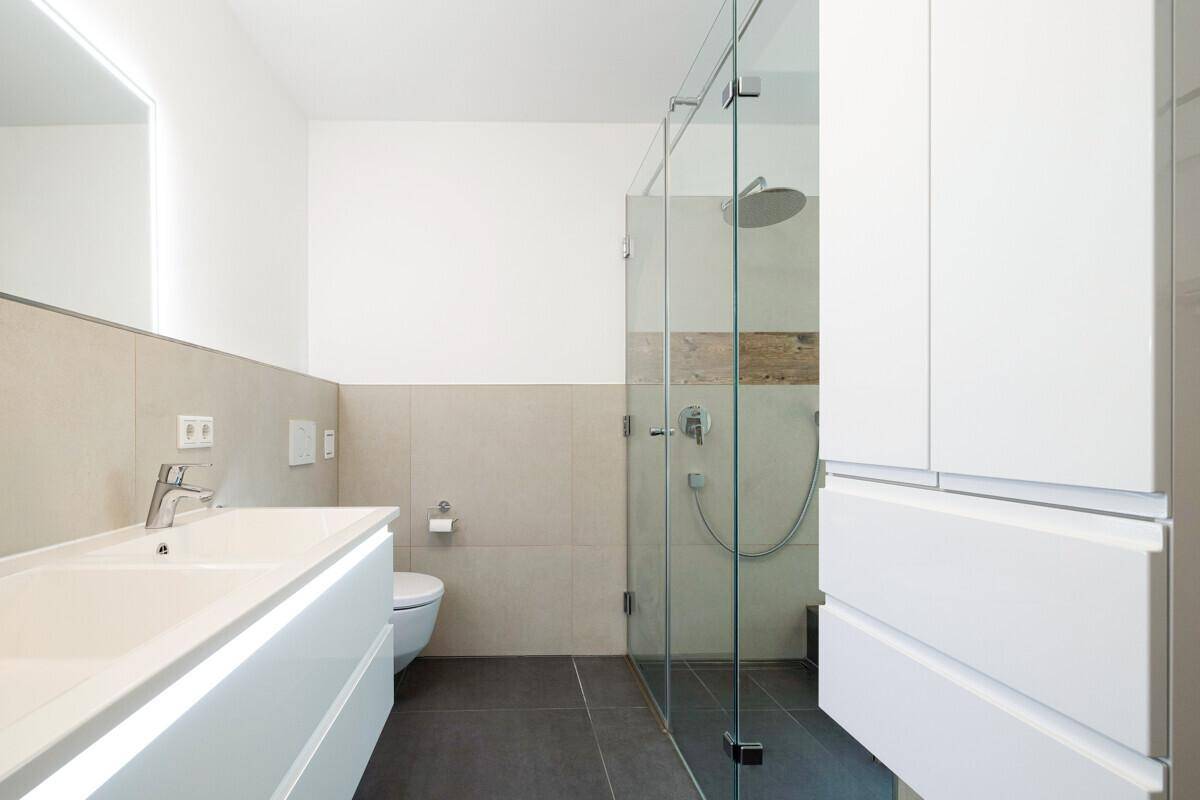 Helles Badezimmer mit modernem Waschtisch, Toilette und großer, begehbarer Duschkabine.