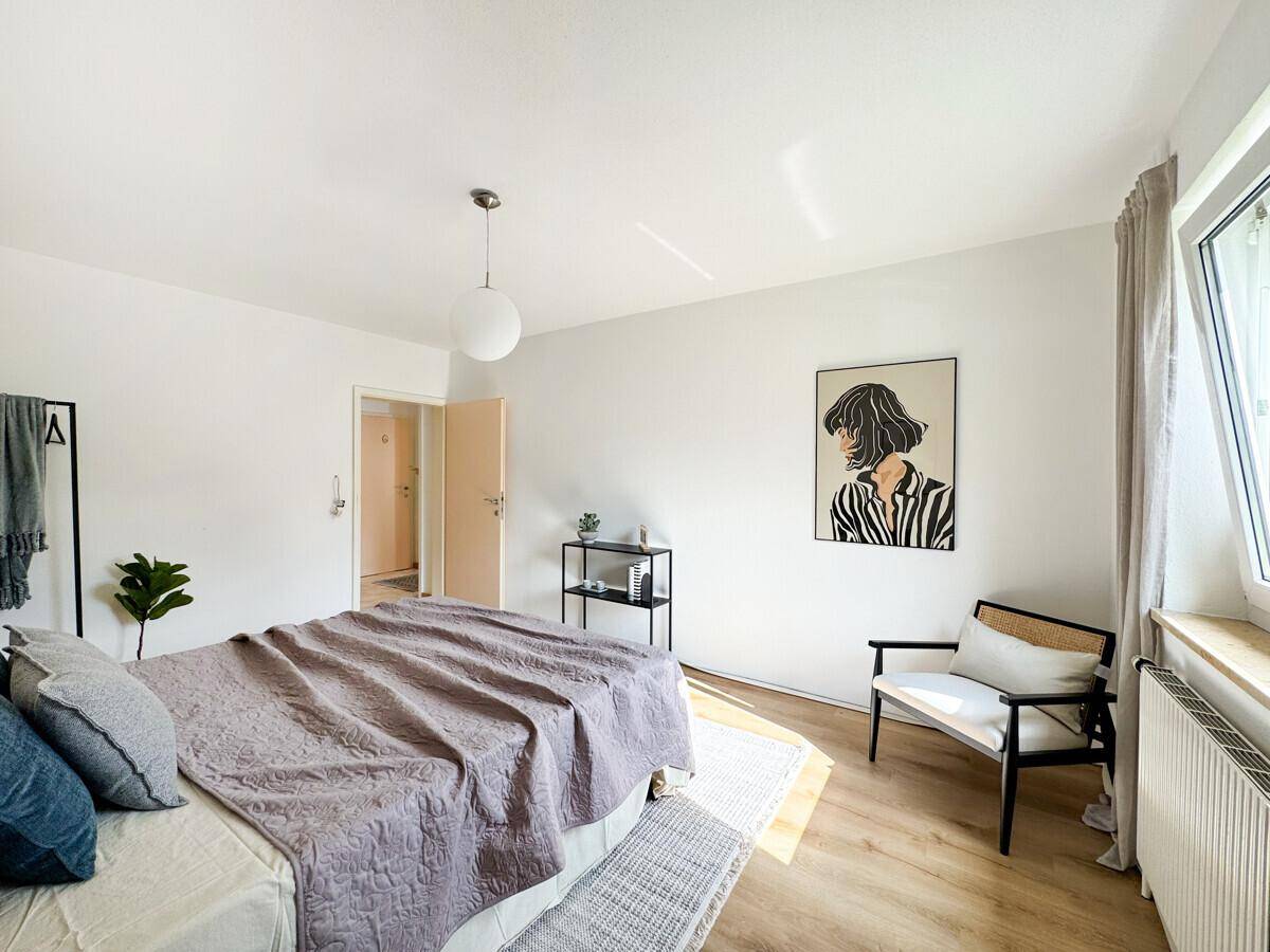 Geräumiges Schlafzimmer mit hellem Laminatboden und minimalistischer Einrichtung.