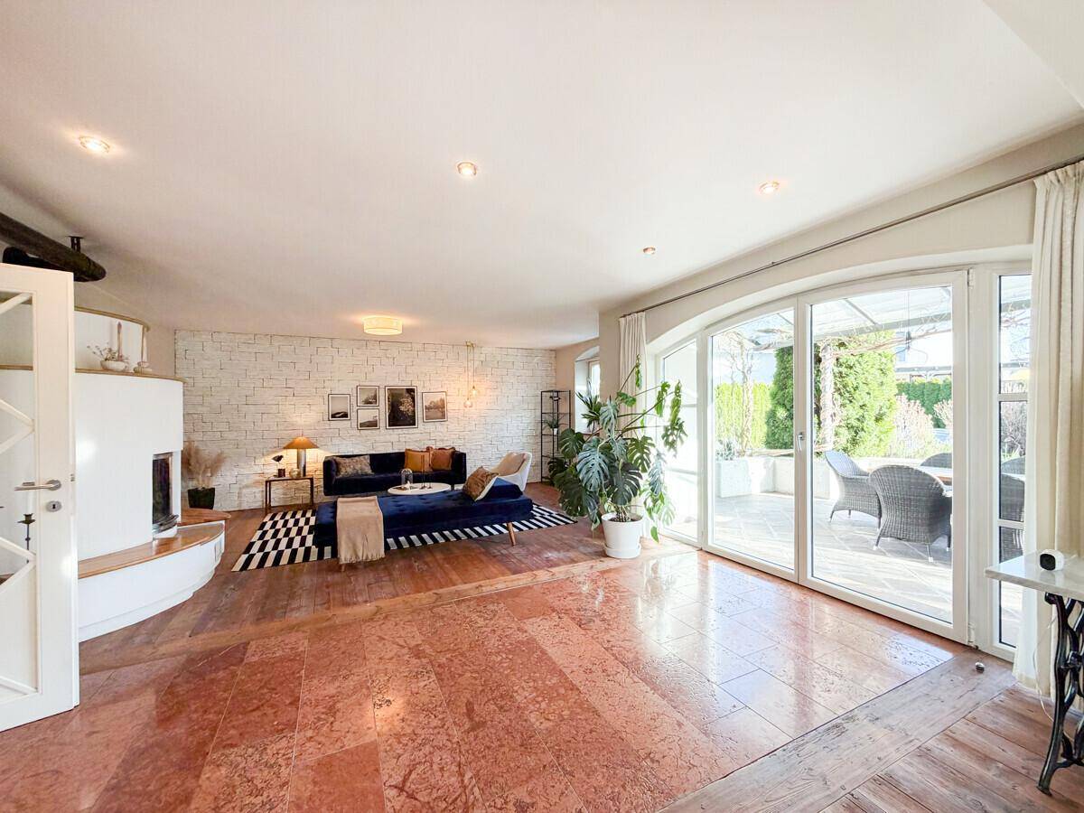 Geräumiges Wohnzimmer mit Kamin, großen Fenstern und direktem Zugang zur möblierten Terrasse.