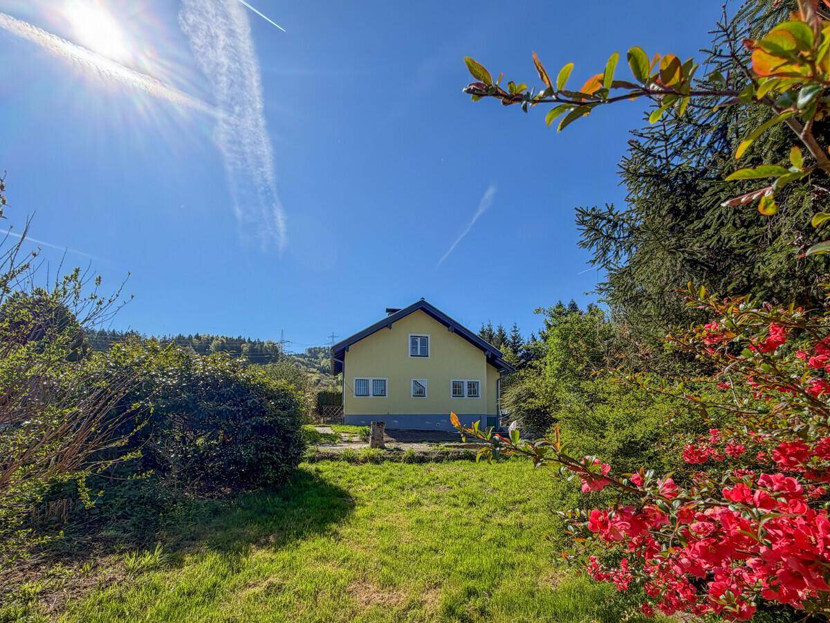 Freistehendes Haus mit gelber Fassade, umgeben von einem großen Garten und Bäumen unter blauem Himmel.