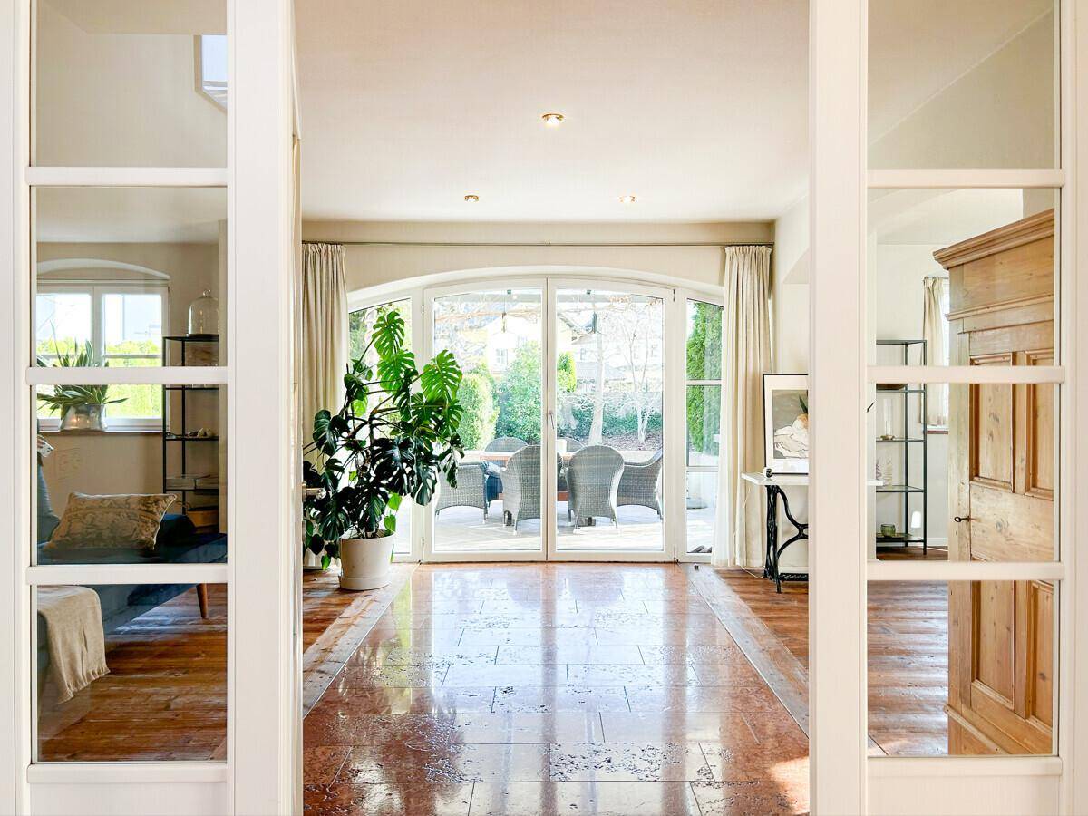 Heller Eingangsbereich mit glänzenden Fliesen und Blick auf die Terrasse und den Garten.