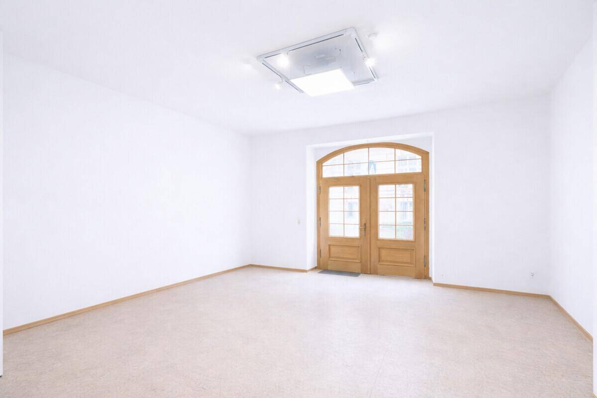 Heller, leerer Raum mit weißen Wänden, beigem Teppichboden und einer großen Holztür mit Bogen.