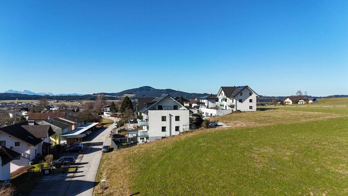Wohngebiet mit modernen Häusern und grünen Wiesen, umgeben von einer bergigen Landschaft.