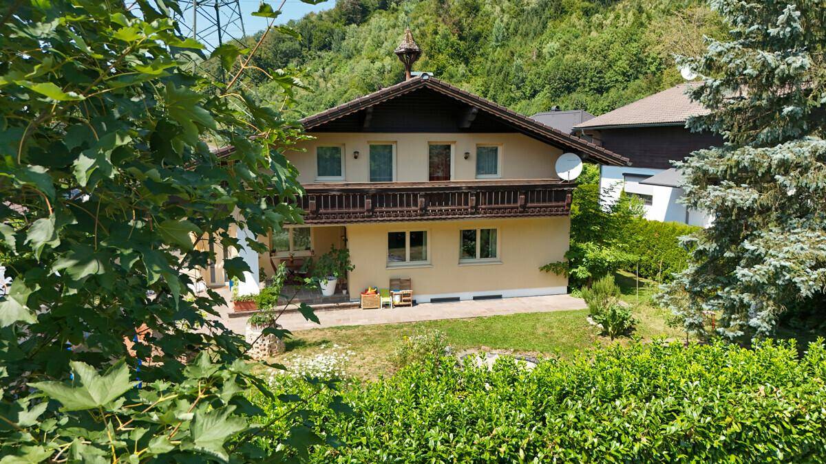 Traditionelles Haus mit Holzbalkon und grüner Umgebung, umgeben von Bäumen.