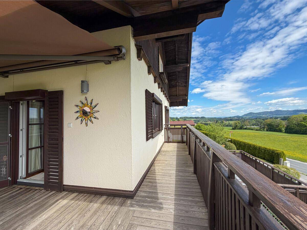 Langer Holzbalkon mit Geländer und Markise, bietet einen weiten Blick über die grüne Landschaft.