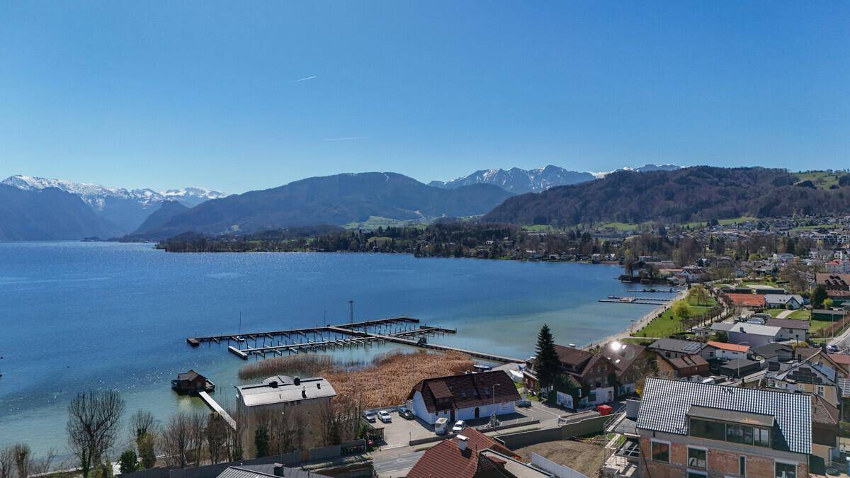 Weitläufiger Blick auf den See mit Yachthafen, die Bergkette und die angrenzende Uferlandschaft.