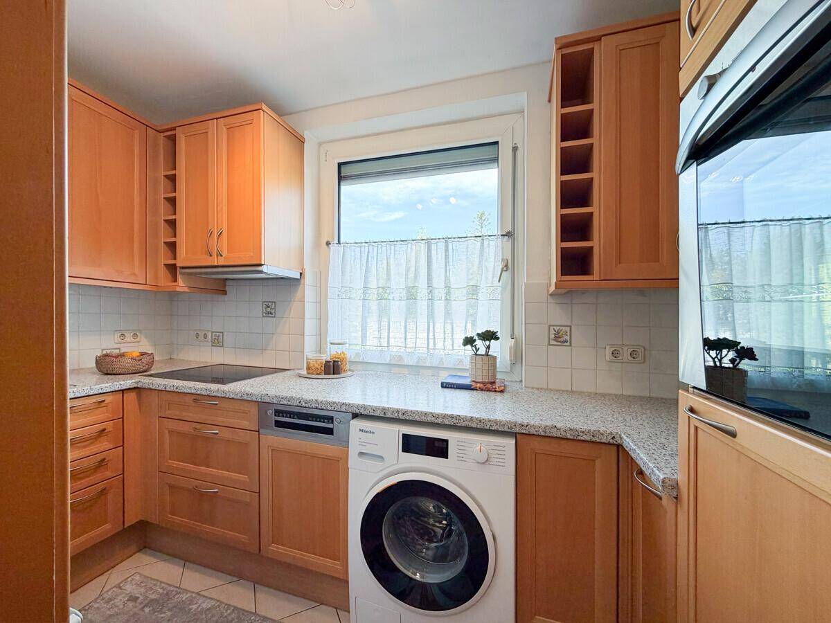 Funktionale Küche mit Holzschränken, integrierter Waschmaschine und Fenster.