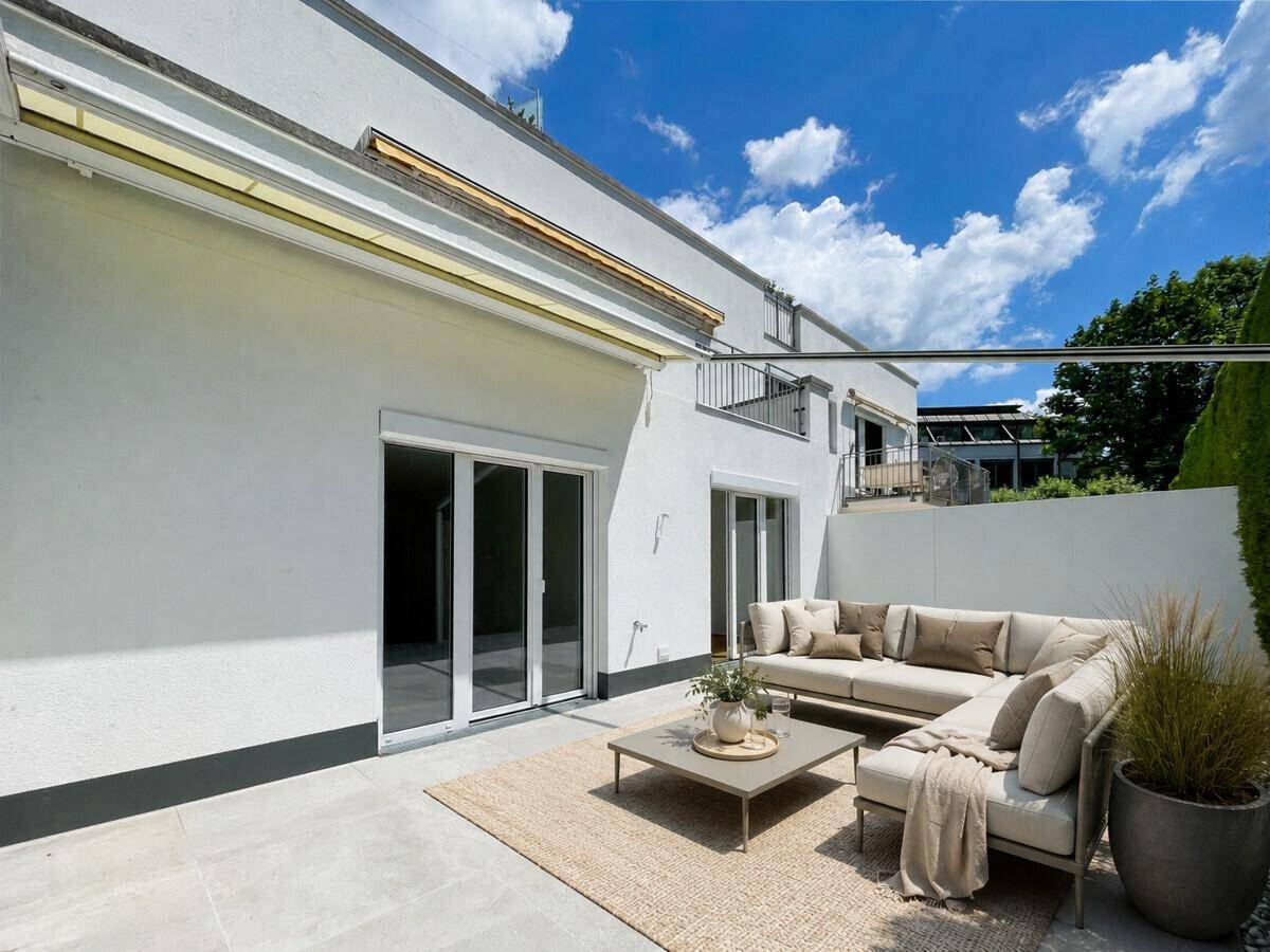 Geräumige Terrasse mit bequemen Loungemöbeln und Markise unter blauem Himmel.