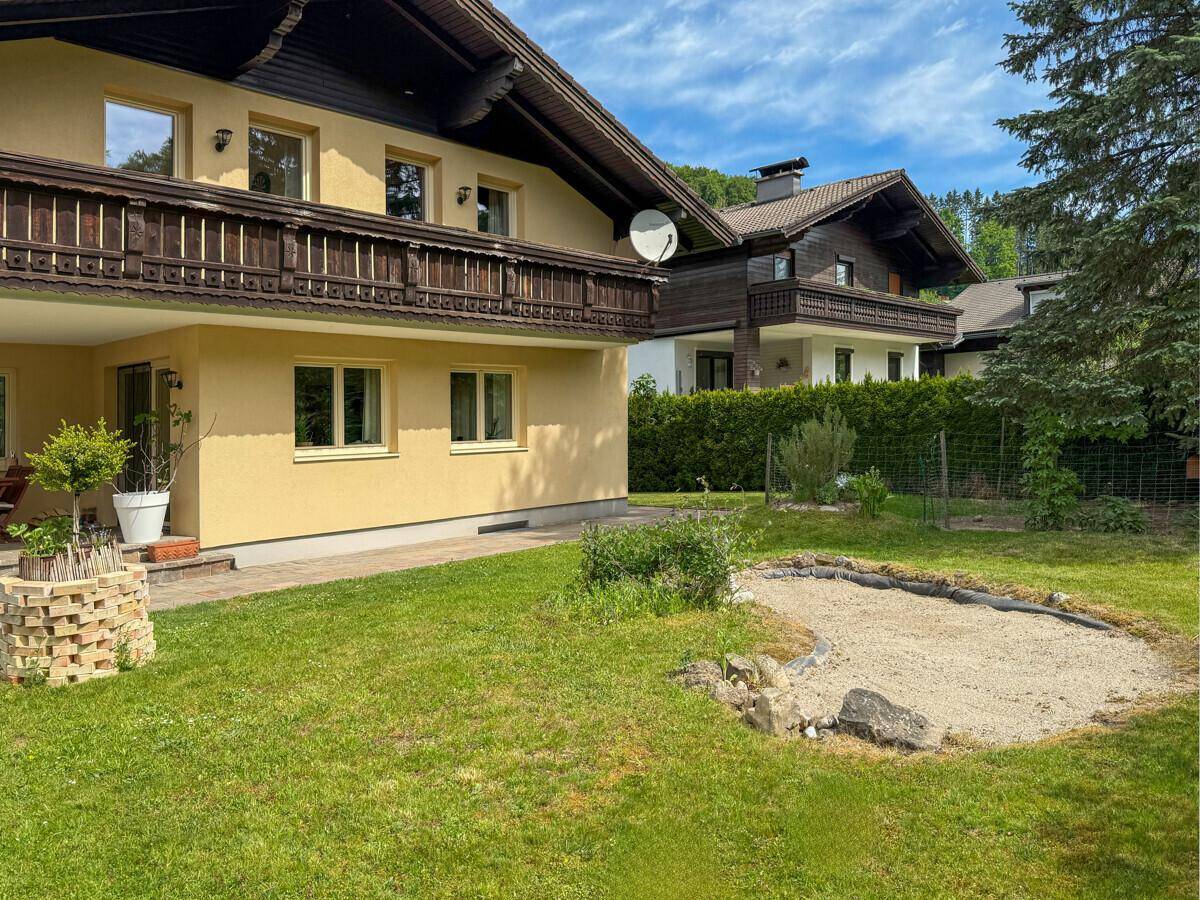Gartenbereich mit Rasenfläche, Sandkasten und Zugang zu einem Holzbalkon.