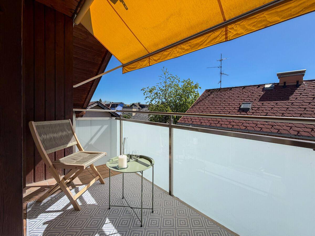 Sonniger Balkon mit Markise, Sitzgelegenheiten und Blick über die Dächer der Nachbarschaft.