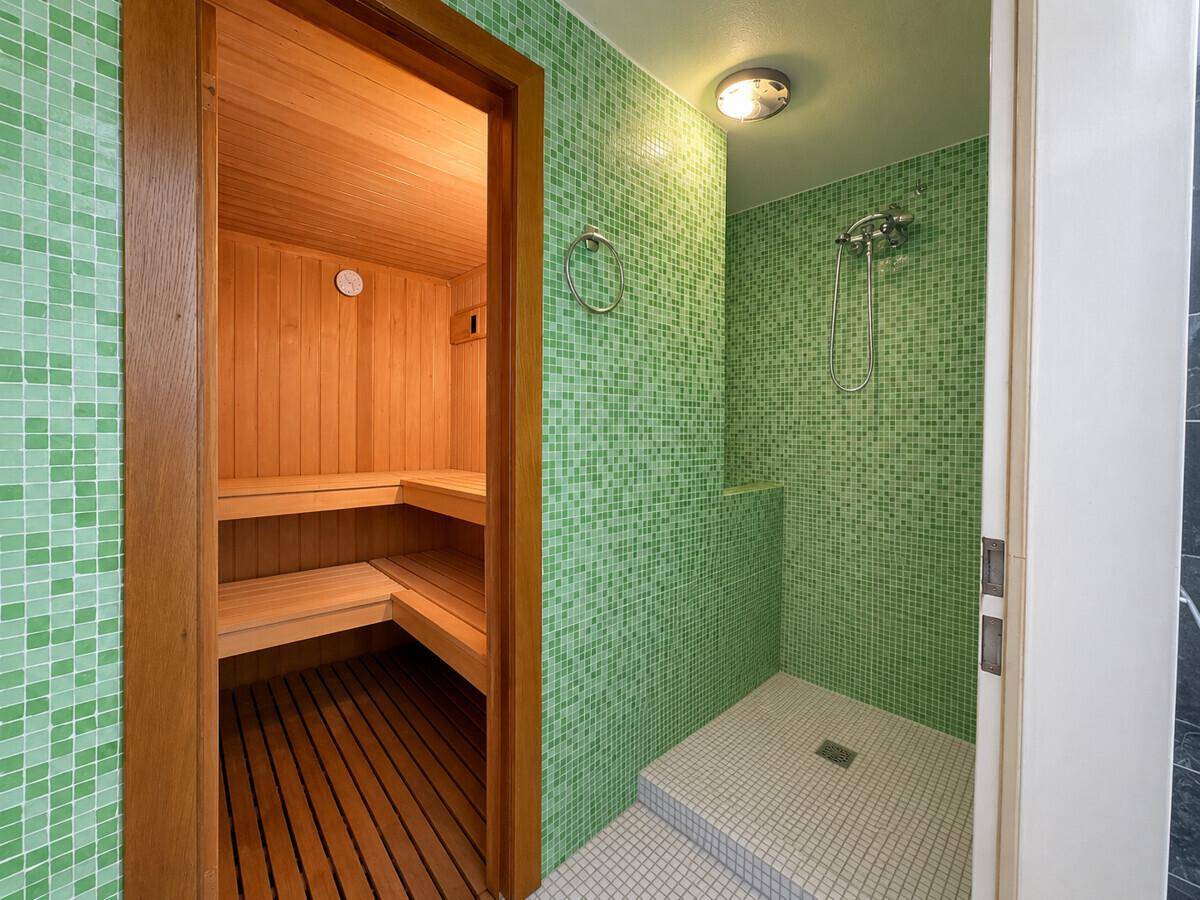 Wellnessbereich mit holzverkleideter Sauna und moderner Dusche mit grünen Mosaikfliesen.