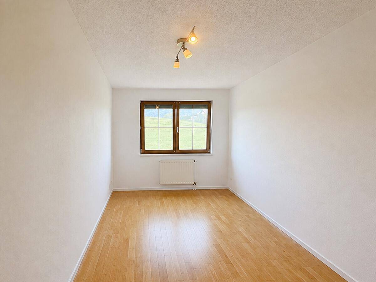 Helles Schlafzimmer mit Holzboden und Blick ins Grüne durch das Fenster.