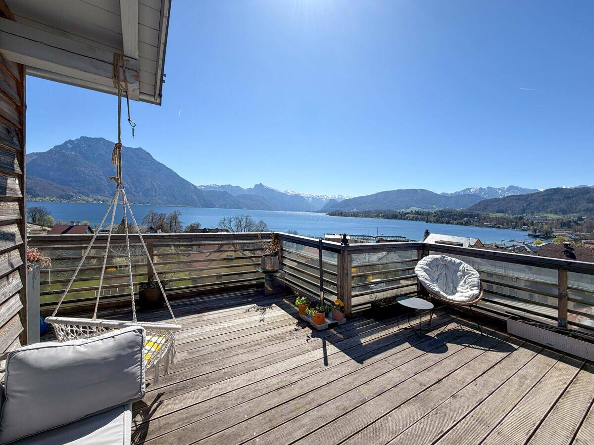Sonnige Holzterrasse mit bequemen Sitzgelegenheiten und atemberaubendem Panorama auf See und Berge.