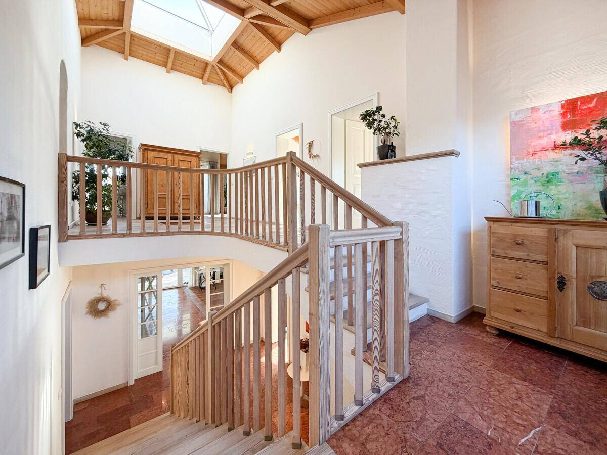 Offenes Treppenhaus mit Holzgeländer, hohen Decken und einem großen Dachfenster für viel Licht.
