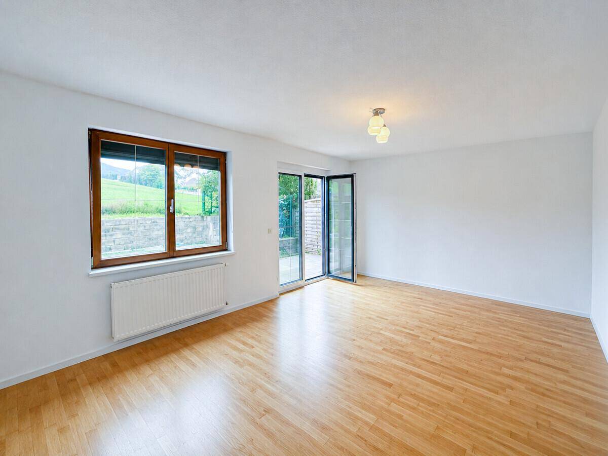 Heller Wohnraum mit Holzboden, großem Fenster und Zugang zur Terrasse.