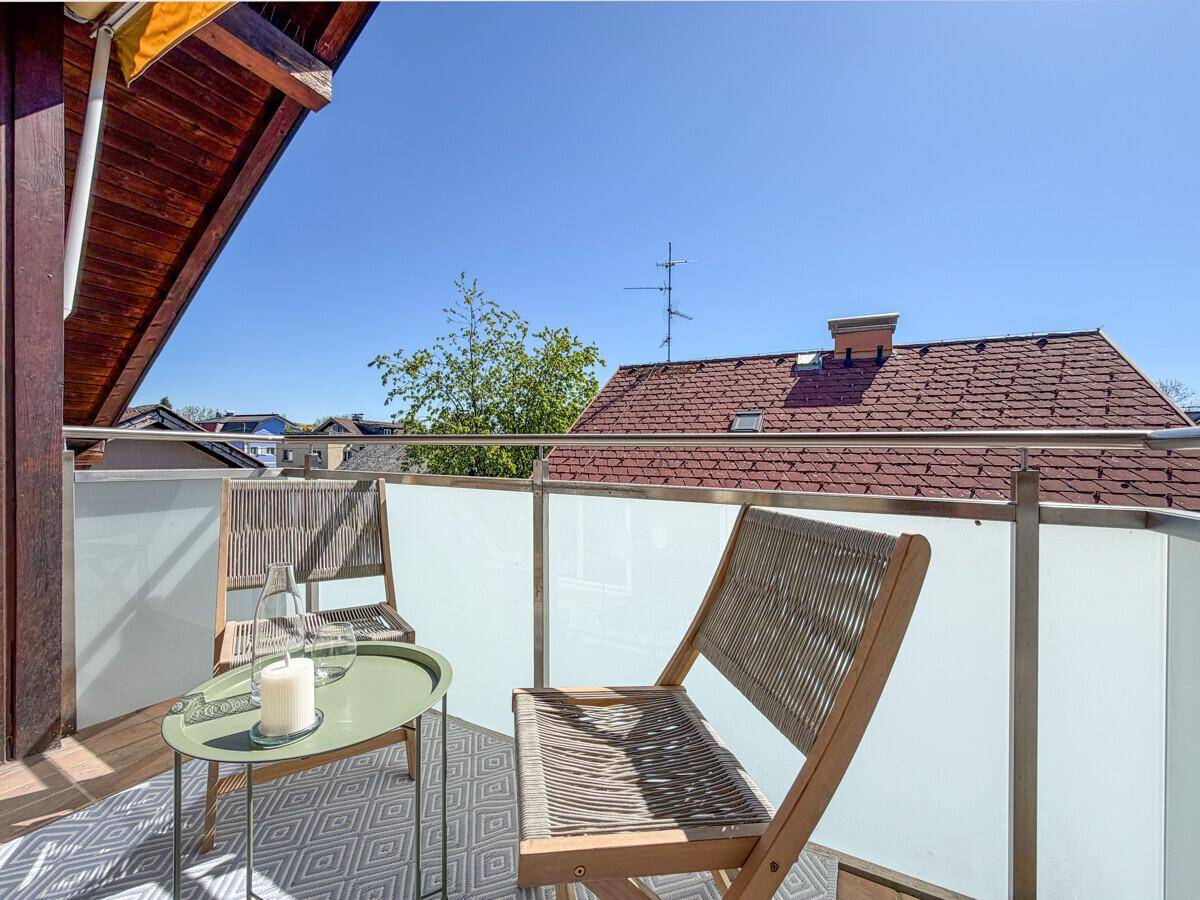 Gemütlicher Balkon mit zwei Stühlen, einem kleinen Tisch und einer Markise unter blauem Himmel.