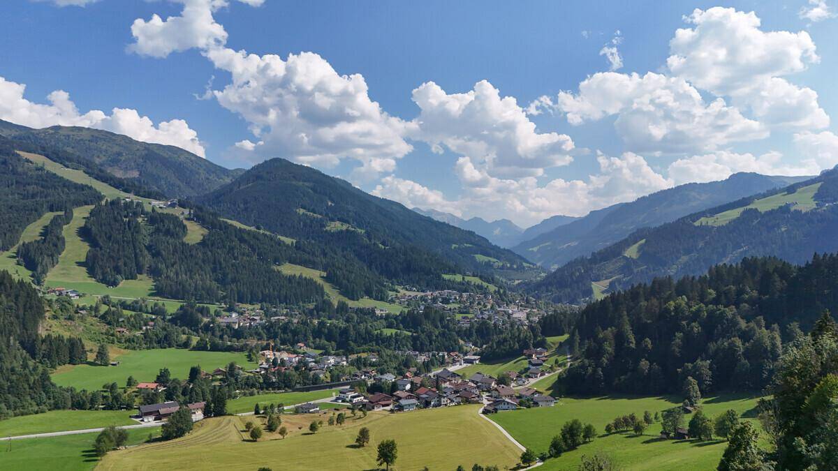 Weitläufiger Panoramablick auf ein malerisches Bergdorf eingebettet in eine grüne Tallandschaft.