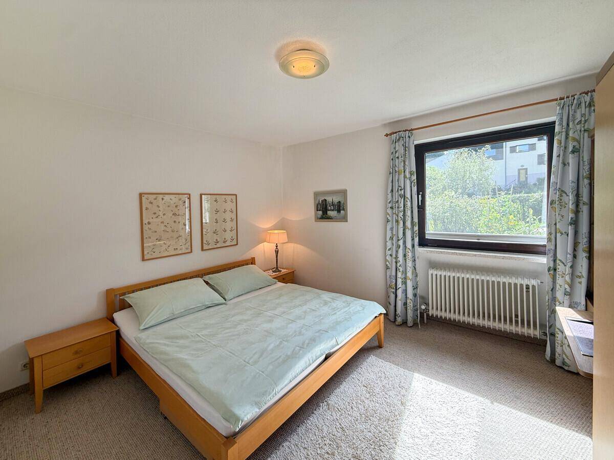 Schlafzimmer mit Teppichboden, Doppelbett und Fenster mit Blick ins Grüne.
