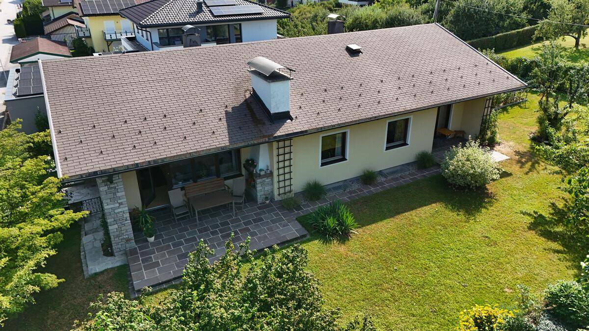 Rückansicht des Hauses mit großer Rasenfläche und gepflasterter Terrasse.