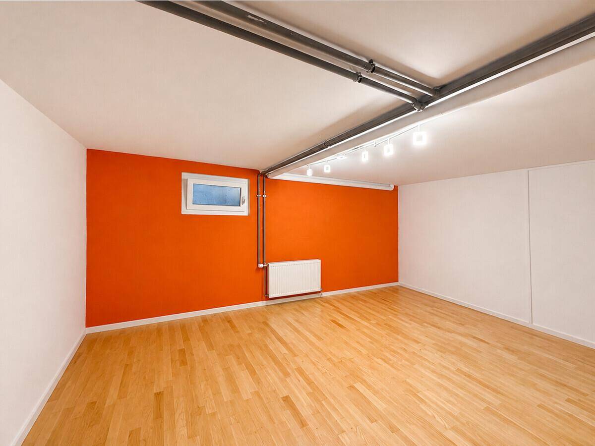Geräumiger Kellerraum mit Holzboden und orangefarbener Akzentwand, gut beleuchtet.