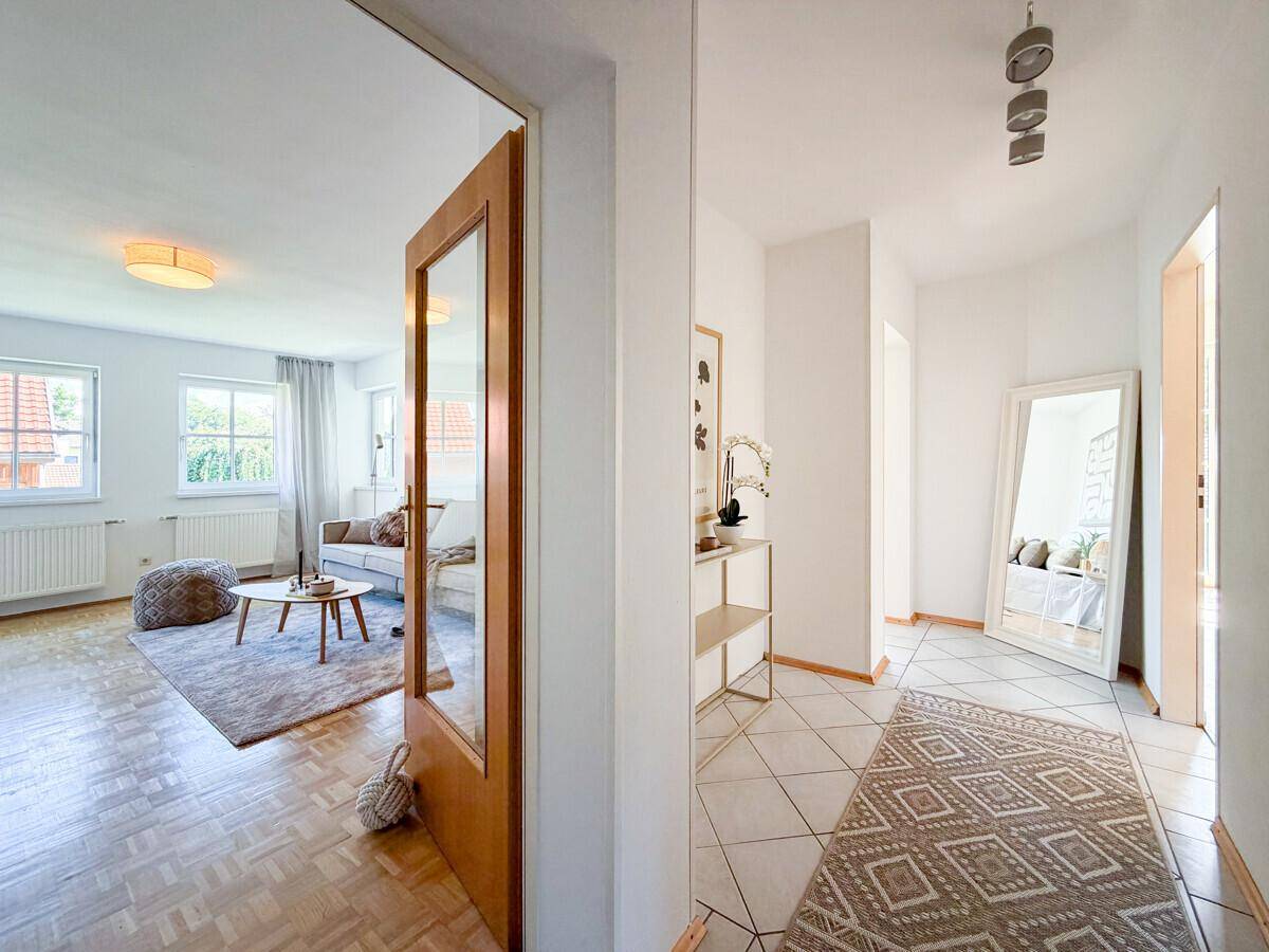 Heller Flur mit Fliesenboden, großem Spiegel und Blick ins Wohnzimmer.